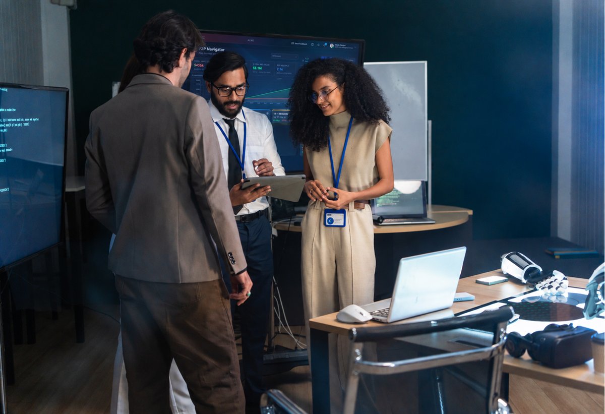 Colleagues reviewing an AI initiative while the AIF P2P Navigator appears on a nearby monitor